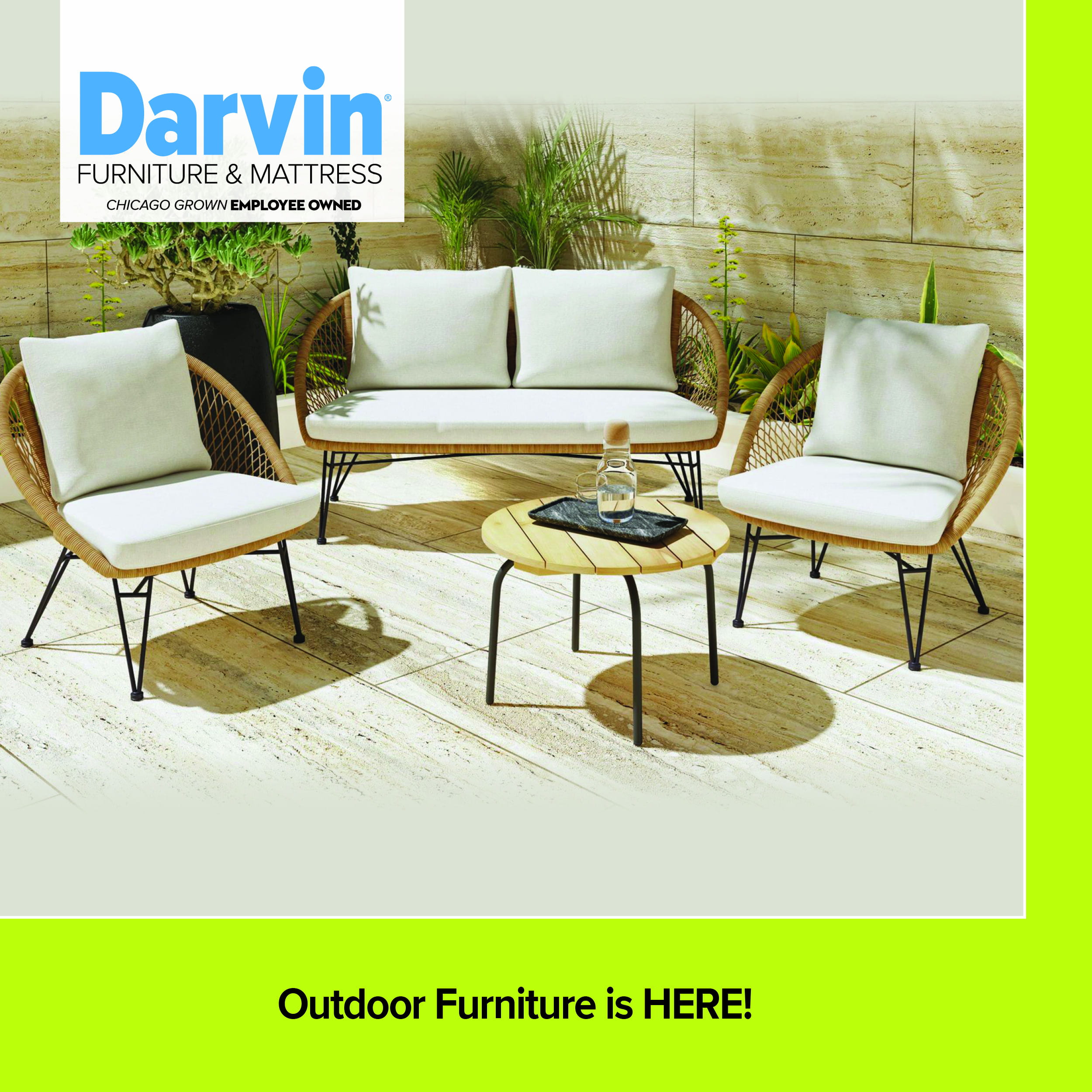 A contemporary outdoor patio set from Darvin Furniture & Mattress, featuring a loveseat and two matching armchairs with light-colored cushions and woven wicker-style backs on black metal legs. A small round wooden slat-top coffee table sits in the center. The set is arranged on a light stone patio with potted plants in the background. A lime green footer reads 'Outdoor Furniture is HERE!'.