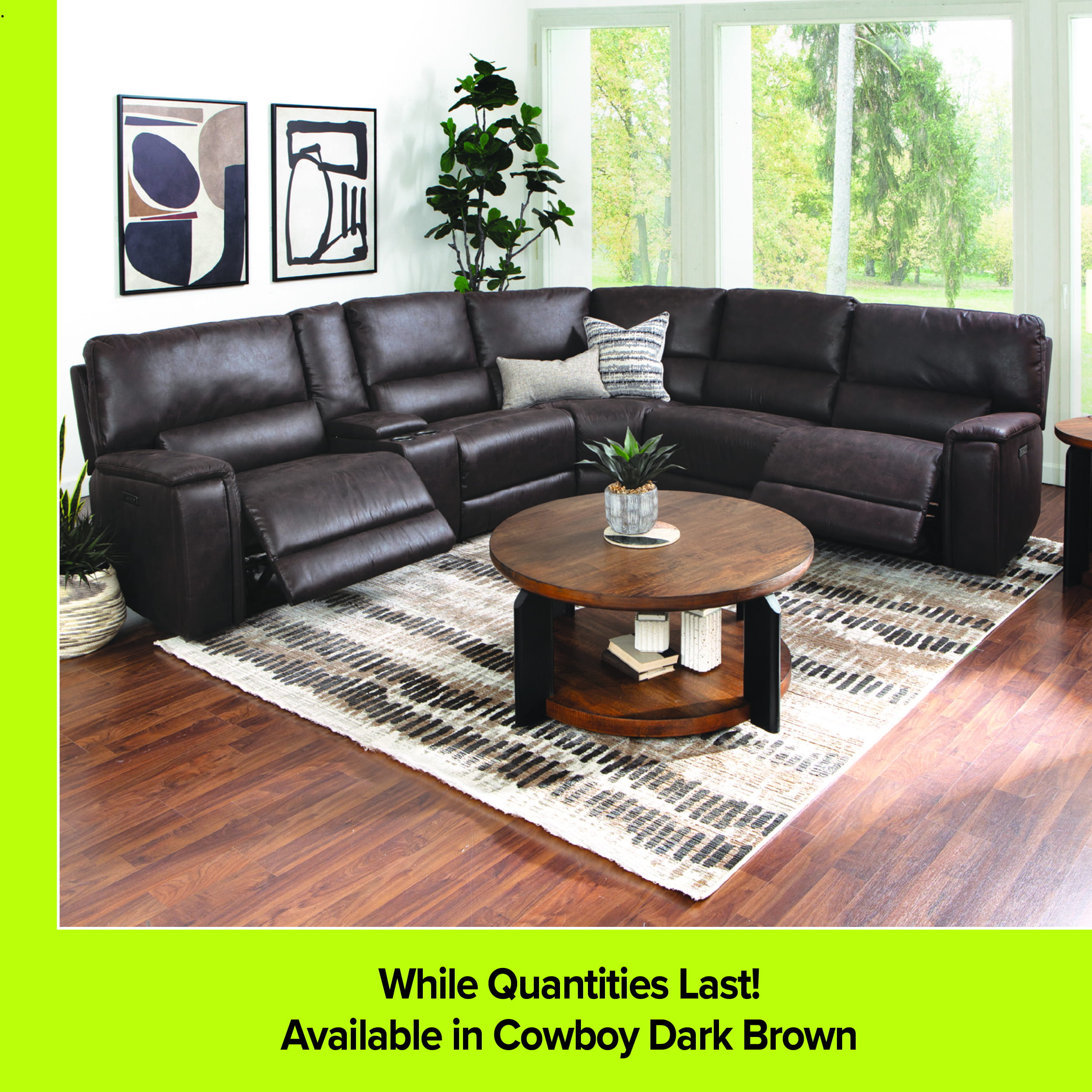 A large dark brown leather reclining sectional sofa, identified as Cowboy Dark Brown, in a modern living room setting. The room includes a round wooden coffee table with a lower shelf, a patterned area rug, two framed abstract art pieces on the wall, and a large window in the background. A lime green footer reads 'While Quantities Last!' and 'Available in Cowboy Dark Brown'.