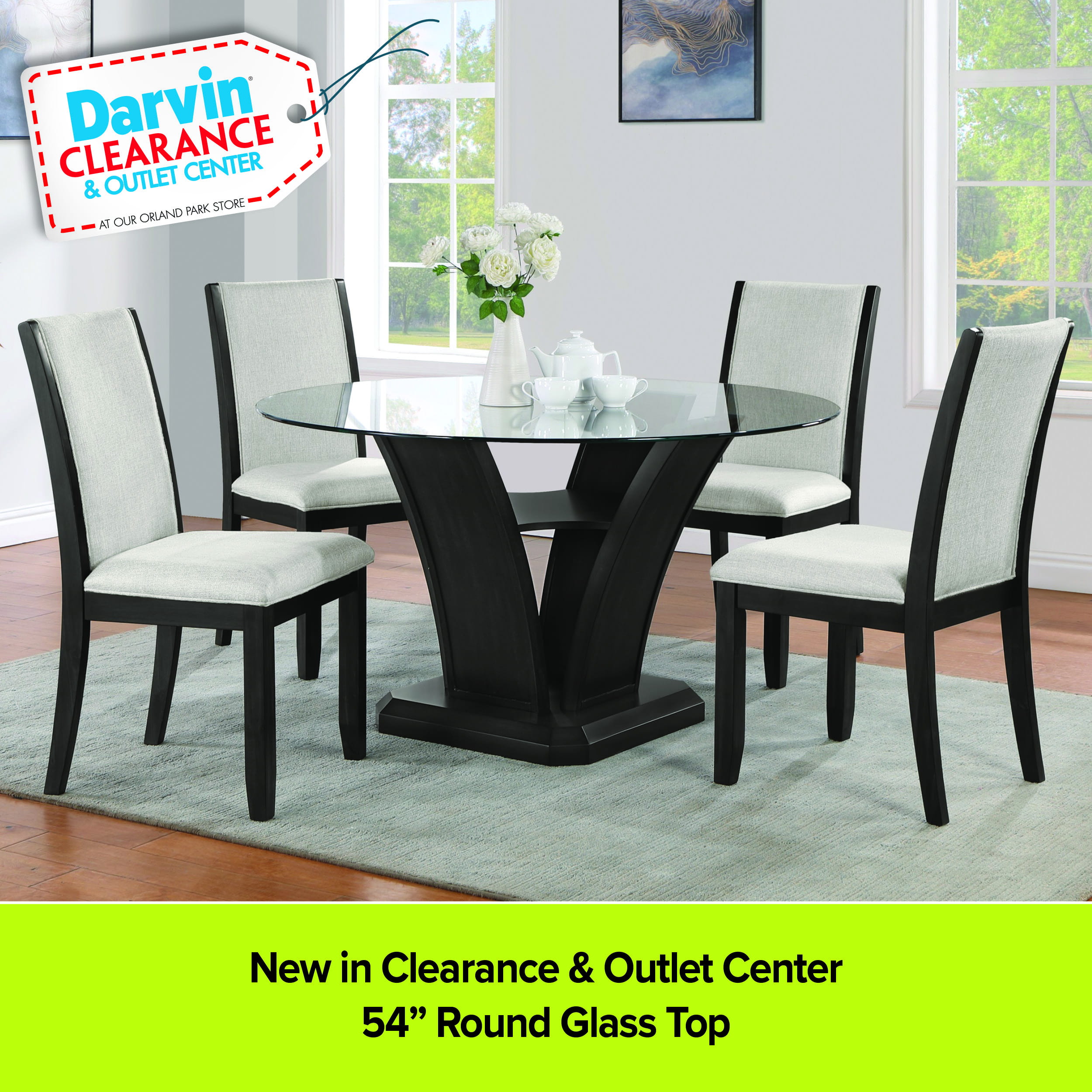 A modern dining set from the Darvin Clearance & Outlet Center featuring a 54-inch round glass-top table with a dark, architectural pedestal base. Four matching chairs with dark wood frames and light grey upholstered seats and backs surround the table on a light blue rug. A Darvin Clearance price tag is in the top left, and a lime green footer reads 'New in Clearance & Outlet Center' and '54” Round Glass Top'.
