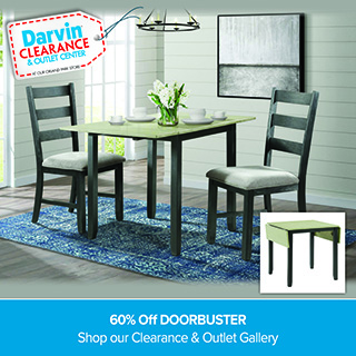 A promotional advertisement for Darvin Clearance & Outlet Center featuring a small dining set. The main image shows a wooden drop-leaf dining table with a light finish top and dark legs, paired with two matching dark-finished ladder-back chairs with upholstered light grey seats. The set sits on a vibrant blue patterned area rug in a bright room with light horizontal wood-paneled walls. An inset photo in the bottom right corner illustrates the table with its drop leaves folded down into a compact square shape. In the upper left corner, a white price tag graphic with a red stitched border reads 'Darvin CLEARANCE & OUTLET CENTER AT OUR ORLAND PARK STORE'. A solid blue banner running along the bottom reads '60% Off DOORBUSTER' followed by 'Shop our Clearance & Outlet Gallery' in clean white text.