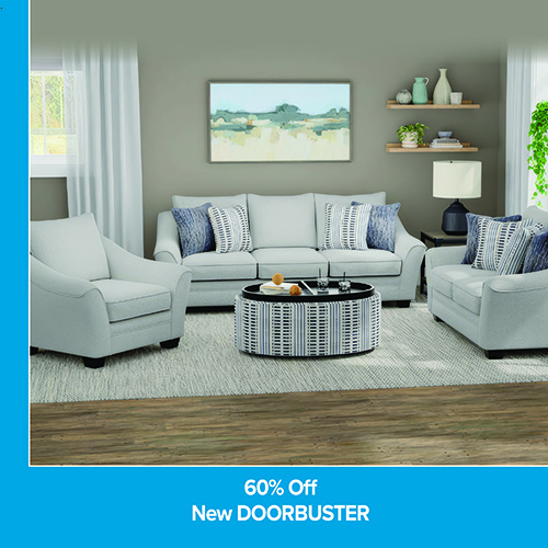 A promotional advertisement featuring a living room furniture set on sale. The image displays a three-cushion sofa, a coordinating two-cushion loveseat, and a matching armchair, all upholstered in a light grey or off-white fabric with flared arms. The furniture is styled with an assortment of blue, white, and textured patterned throw pillows. In the center sits a large, oval cocktail ottoman upholstered in a blue and white vertical stripe pattern, topped with a black tray holding decorative accents. The set rests on a light grey textured area rug over a wood-look floor. In the background, a muted green landscape painting hangs on a grey wall next to two floating wooden shelves. A solid blue banner along the bottom reads '60% Off' followed by 'New DOORBUSTER' in bold white text, with a matching blue vertical border framing the left side.