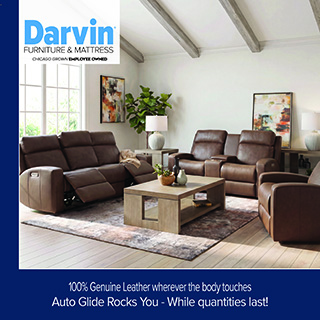 A promotional advertisement for a leather living room furniture collection at Darvin Furniture & Mattress. The image displays a matching brown leather reclining living room set, including a three-cushion reclining sofa shown with its footrests extended, a two-cushion reclining loveseat with a center console, and a matching armchair. The furniture pieces are arranged around a light natural wood coffee table with open end panels, resting on a brown and grey textured area rug over light hardwood flooring. The room is bright with white walls, vaulted ceilings featuring exposed grey wooden beams, a large window on the left, and a potted green plant in the background. The Darvin Furniture & Mattress logo sits in a white block in the upper left corner. A dark blue banner runs along the bottom with white text that reads, '100% Genuine Leather wherever the body touches' stacked above 'Auto Glide Rocks You - While quantities last!'.