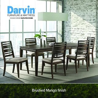 Darvin Furniture & Mattress logo above a dark wood dining table with six upholstered ladder-back chairs, pendant light fixture, in a room with a brick accent wall. Text reads Brushed Mango finish.