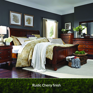 Bedroom with a dark cherry wood sleigh bed with gold and white bedding, matching nightstands and dressers, framed art, and a dark blue accent wall. Text reads Rustic Cherry finish.