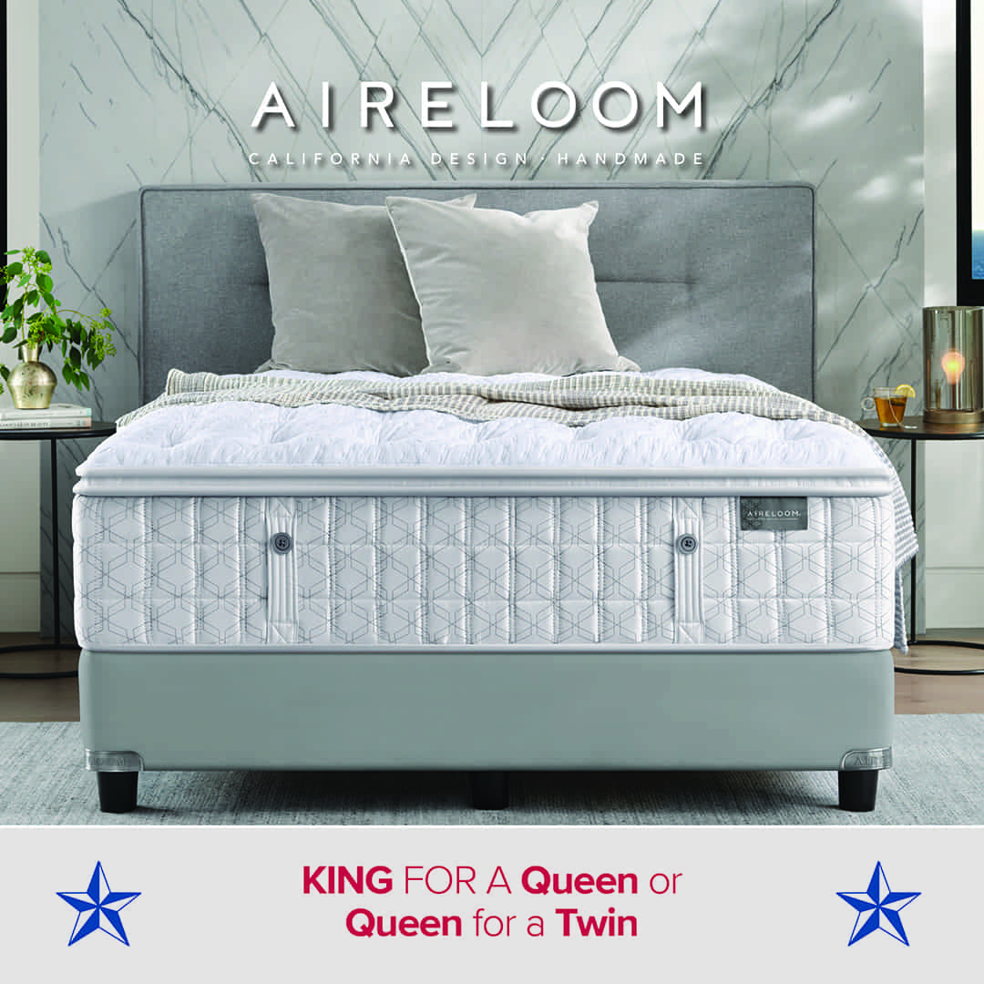 A modern bedroom setup featuring an Aireloom mattress with a geometric quilted pattern on a light gray bed frame and headboard. The bed is neatly made with white bedding, gray pillows, and a soft blanket. A side table with a drink, candle, and lamp sits beside the bed, with plants and marble-patterned walls in the background. Text on the image reads: “AIRELOOM – California Design / Handmade” and “KING for a Queen or Queen for a Twin,” with blue stars on each side.