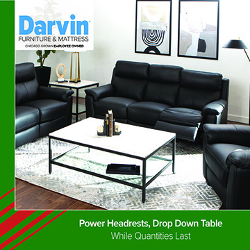 A promotional image from Darvin Furniture & Mattress showing a modern living room setup with black leather sofas arranged around a white rectangular coffee table with a black metal frame. The room includes framed artwork on the wall, a floor lamp, and a light-colored patterned rug. Text at the bottom reads: Power Headrests, Drop Down Table — While Quantities Last.