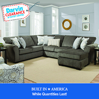 Promotional image from the Darvin Clearance & Outlet Center showing a large gray sectional sofa with multiple accent pillows in a staged living room with light blue walls, framed artwork, and side tables. A blue banner at the bottom reads “Built in America — Built to Last!”