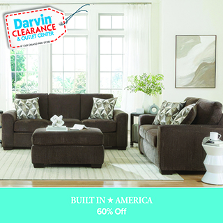 A promotional advertisement for Darvin Clearance & Outlet Center featuring living room furniture. The image displays a dark brown upholstered three-cushion sofa and a matching two-cushion loveseat arranged in a bright living room with large windows. A matching dark brown rectangular ottoman sits in the foreground. The sofa and loveseat are styled with silver and grey geometric patterned throw pillows. In the upper left corner, a white price tag graphic with a red stitched border reads 'Darvin CLEARANCE & OUTLET CENTER AT OUR ORLAND PARK STORE'. A solid teal banner along the bottom features the text 'BUILT IN ★ AMERICA' in a white serif font, followed by '60% Off' in a clean white sans-serif font.