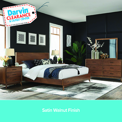 A promotional advertisement for a brown leather motion furniture set. The image showcases a living room arranged with a reclining sofa, a reclining loveseat with a center console dropped down to reveal cup holders, and a matching reclining armchair. The furniture is upholstered in 100% genuine brown leather. A dark wood coffee table rests in the center on a grey distressed area rug. The bright room has large windows looking out at green trees. A solid teal banner along the bottom reads '100% Genuine Leather wherever the body touches' followed by 'Power Headrest, ZeroGravity, Drop Down Table + Speakers' in white text.