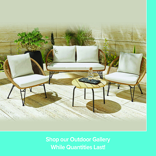 A promotional advertisement for an outdoor patio furniture gallery. The image displays a stylish outdoor conversational set arranged on a light stone tiled patio against a matching stone wall accented with green plants. The set includes a light-colored woven wicker loveseat and two matching armchairs, all topped with plush off-white cushions. A round, light-wood slatted coffee table sits in the center with a water carafe and glass on a black tray. A solid teal banner along the bottom reads 'Shop our Outdoor Gallery' followed by 'While Quantities Last!' in white text.