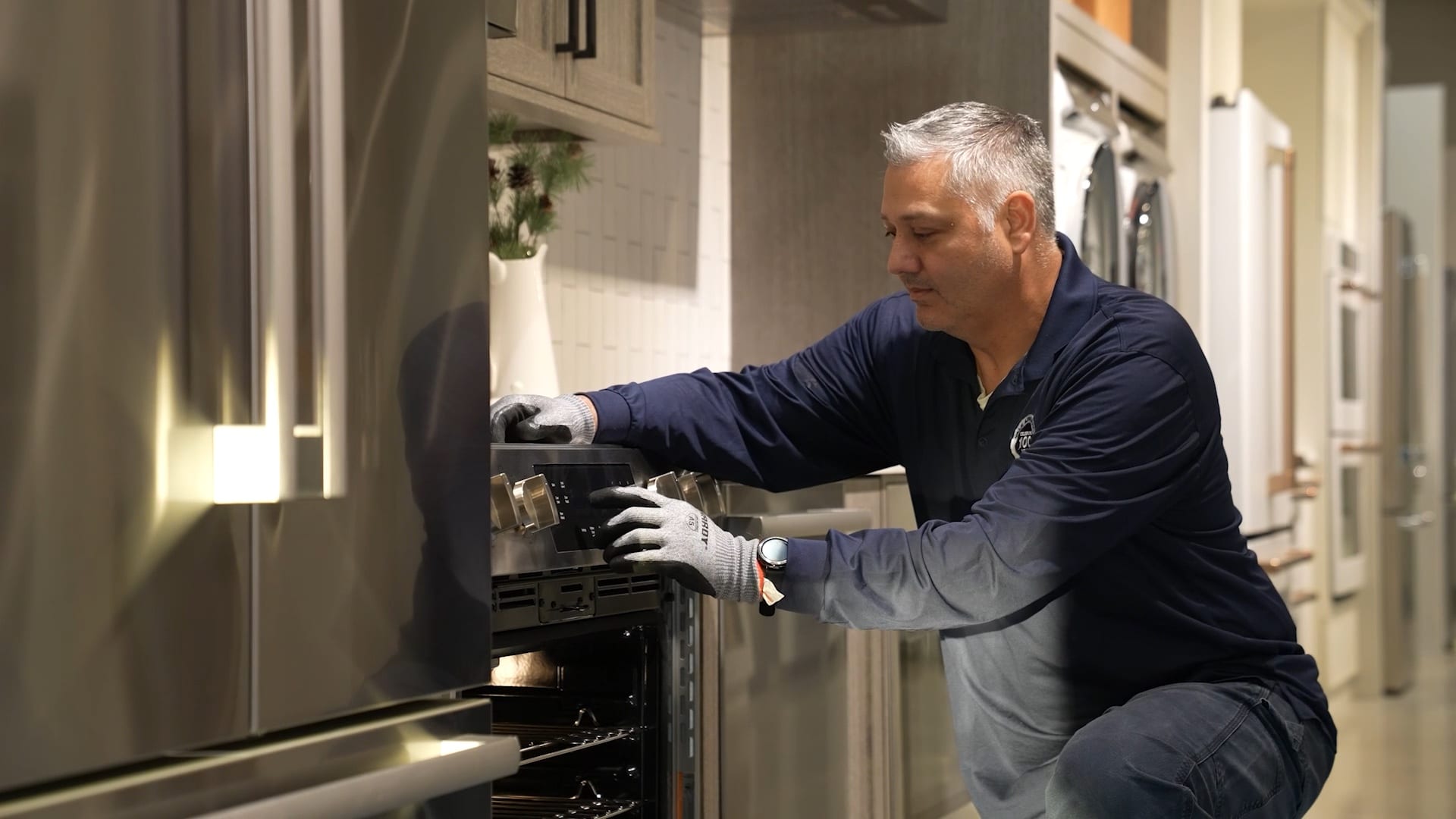 A Yale Appliance service technician working at an open range, both gloved hands on the appliance.