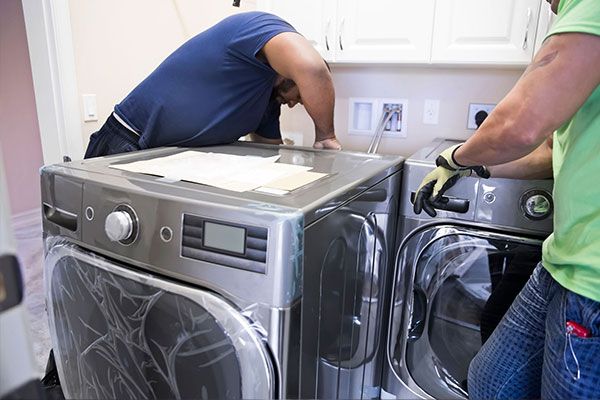 Two men installing a washer & dryer into home