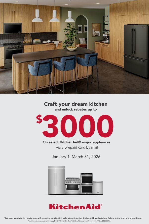Modern kitchen with light wood cabinetry, a large island with blue upholstered stools, pendant lights, and black KitchenAid appliances. Promotional text reads: “Craft your dream kitchen and unlock rebates up to $3000 on select KitchenAid major appliances via a prepaid card by mail. January 1–March 31, 2026.” Images of stainless steel appliances appear above the red KitchenAid logo, with fine print rebate details at the bottom.