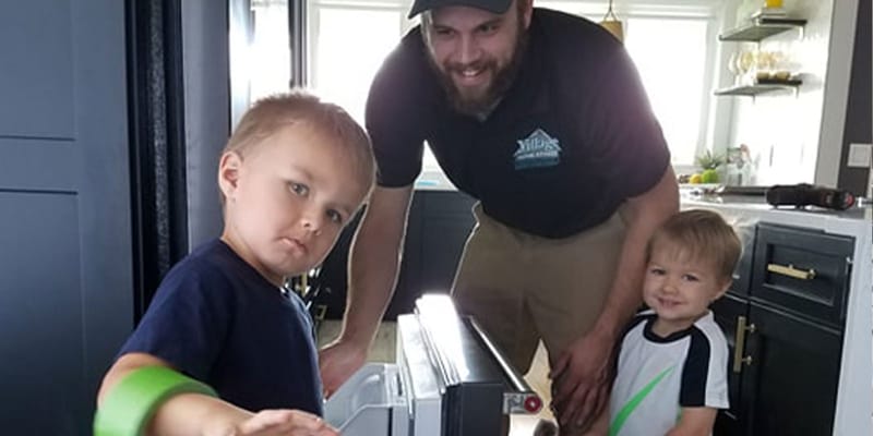 Village Home Stores technician servicing an appliance with two young helpers
