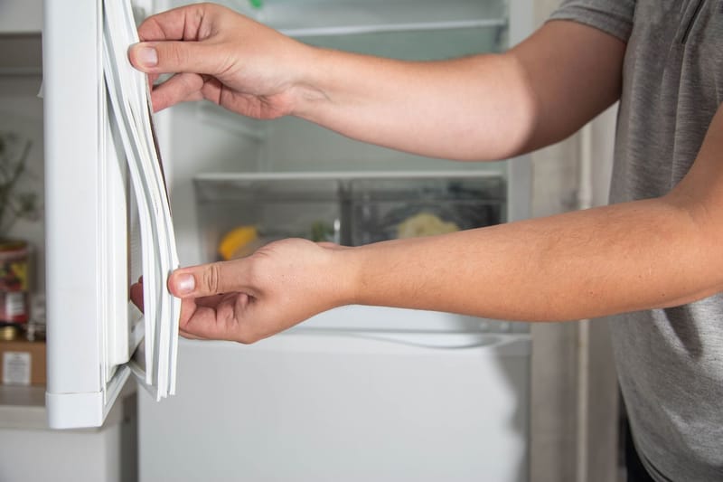 Homeowner checking a refrigerator door seal in a Maine kitchen ahead of fall hosting season