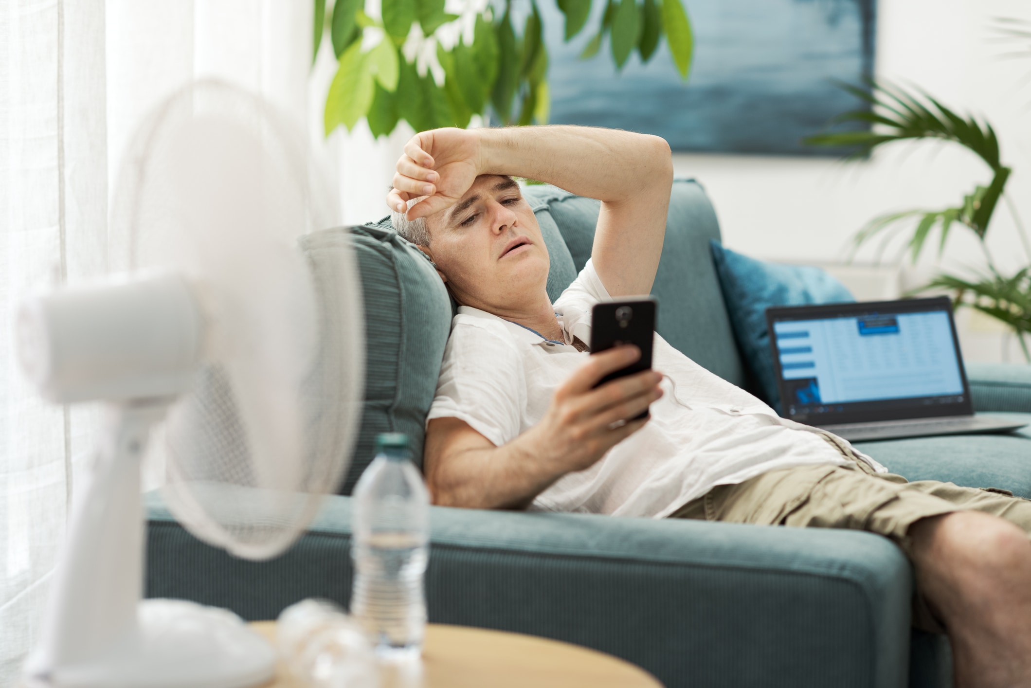 man sitting on a couch overheated with a fan
