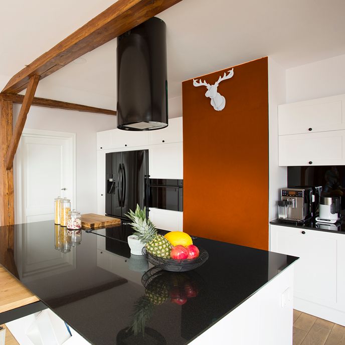White kitchen with black appliances and an orange accent wall and wooden deer head mounted to it. A bowl of fruit is sitting on the black countertop.